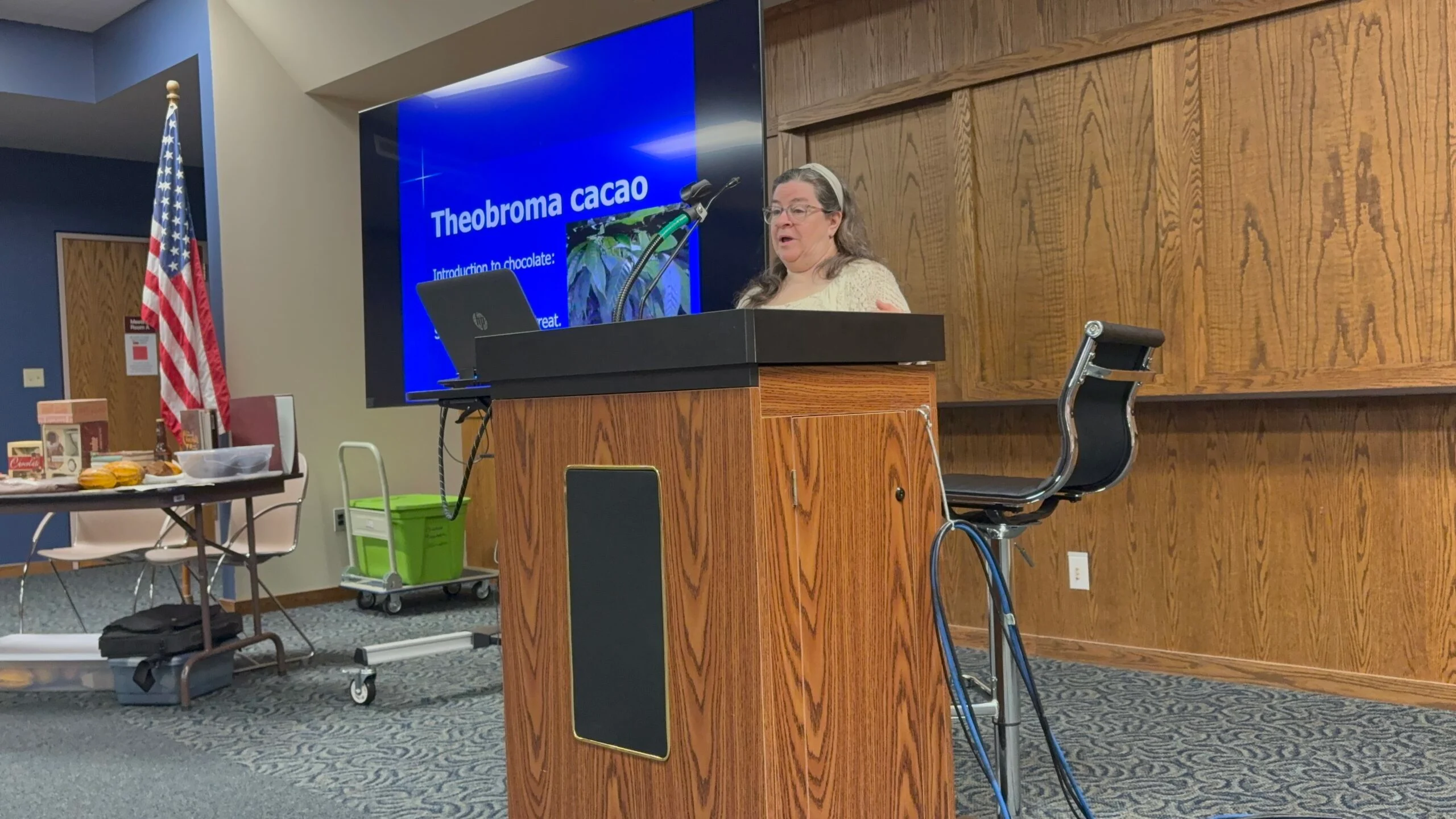 Sheri Ann Richerson presenting a lecture on Theobroma cacao at a podium with a slideshow in the background.